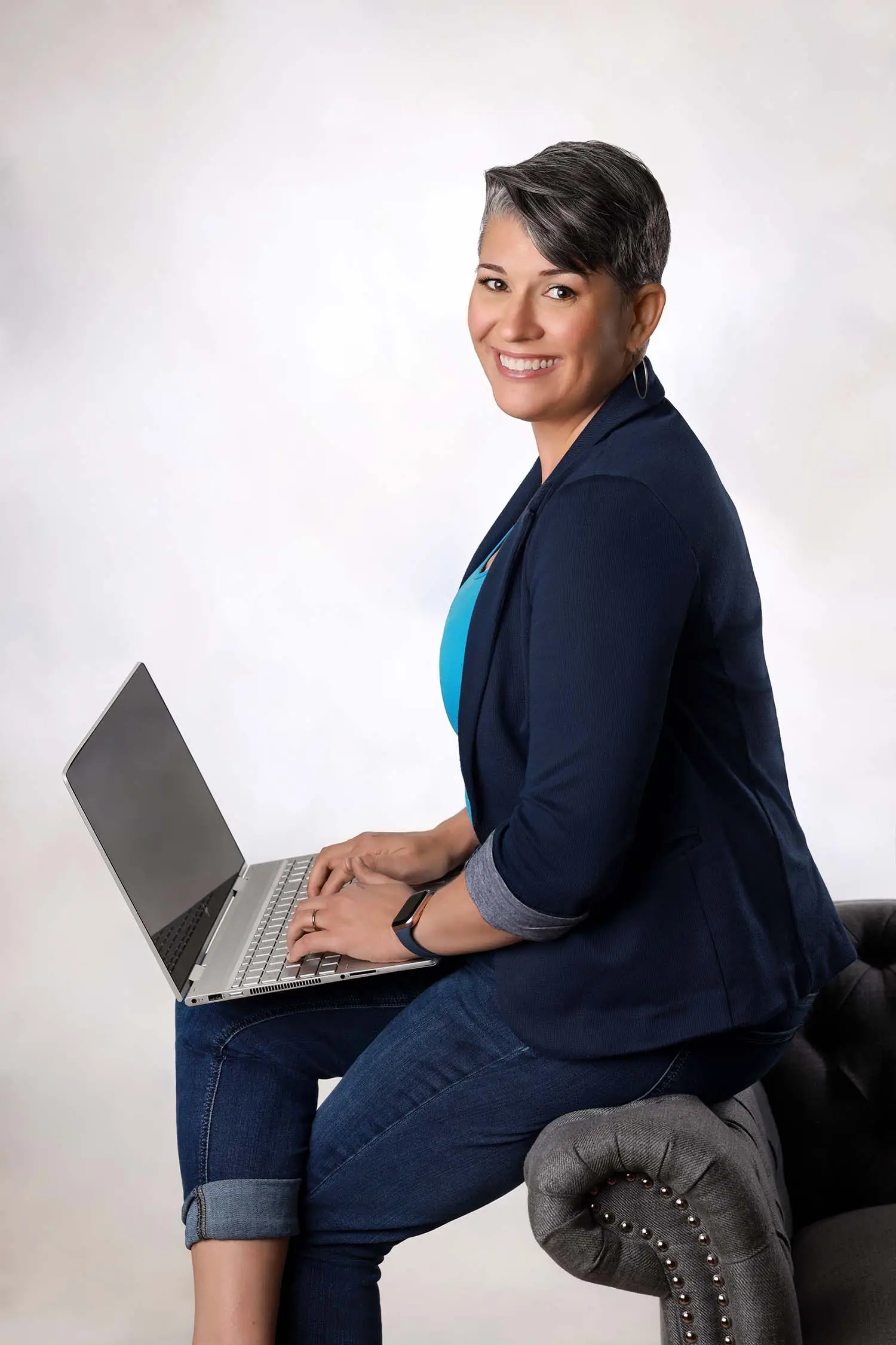 andrea-goulet-2 Andrea Goulet headshot sitting on the edge of a sofa typing on a computer